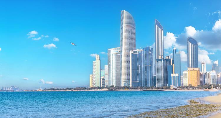 Moderne Skyline von Abu Dhabi, die sich an einem klaren Tag neben einem ruhigen blauen Meer erhebt.