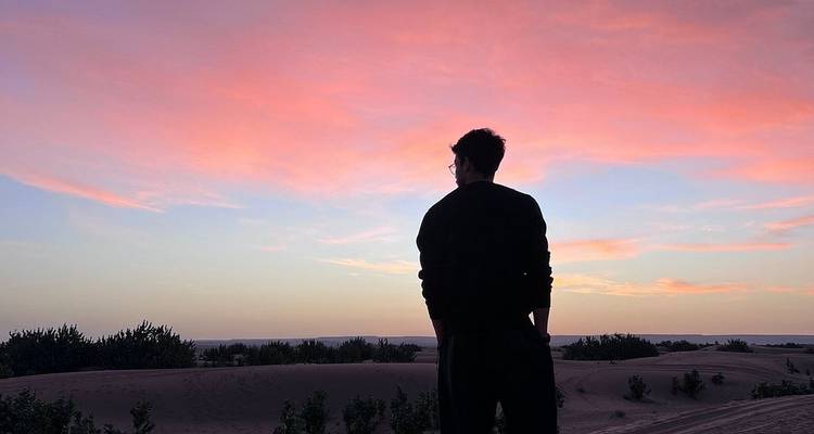 Silhouet van een man staat op een duin onder levendige roze en blauwe zonsondergangwolken