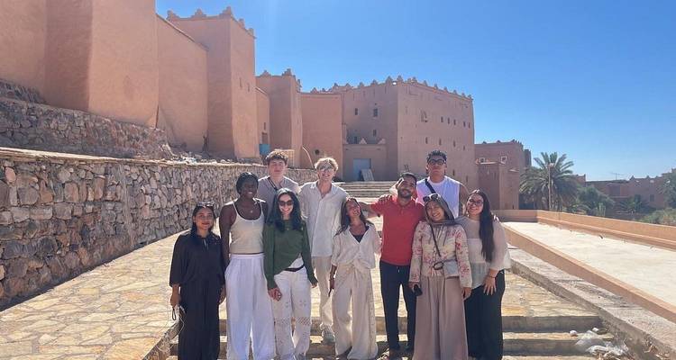 Toergroep poseert in het felle zonlicht buiten een historische adobe kasbah met heldere blauwe luchten