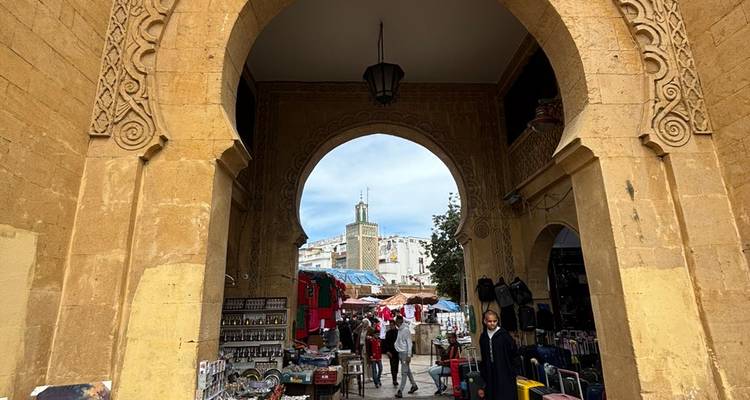Stone gateway leading into a bustling souk with shops and a distant minaret visible through the arch.