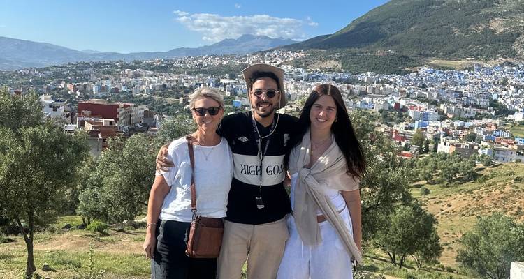 Three travelers smiling with panoramic view of Chefchaouen’s blue buildings spread across hillside