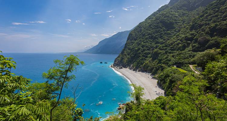 Dramatische, grüne Steilküste, die zu einem abgelegenen weißen Strand und azurblauen Meer abfällt.