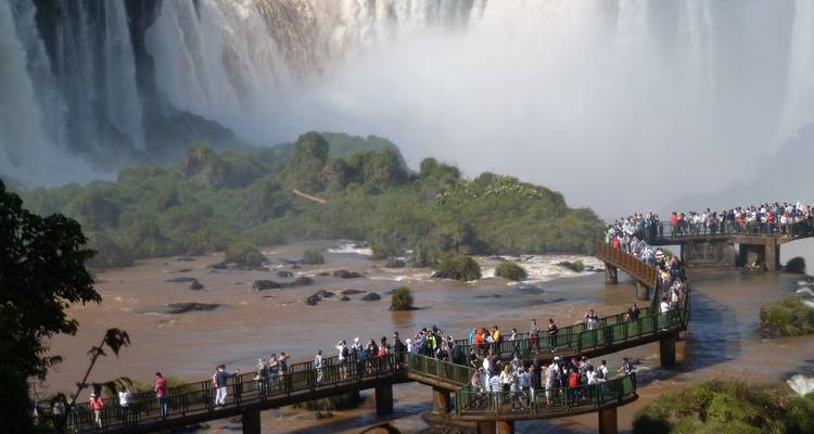 Las multitudes caminan por pasarelas elevadas junto a las poderosas Cataratas del Iguazú con neblina elevándose por todas partes.