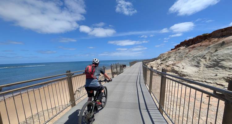 Ein Radfahrer genießt eine Strandpromenade mit Blick auf das ruhige blaue Meer und Sandsteinklippen an einem sonnigen Tag.