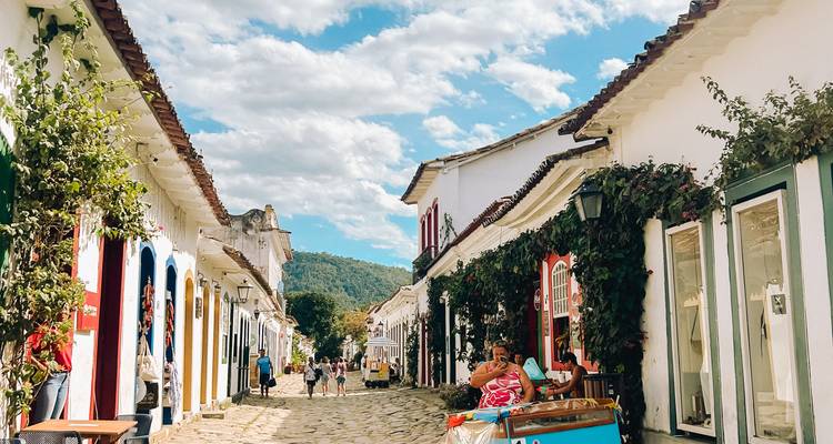 Cobblestone street of Paraty lined with colorful shops and tourists under blue sky.