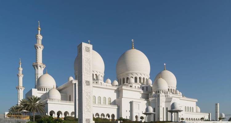 Glänzend weiße Großmoschee mit aufragenden Minaretten und großen Kuppeln vor tiefblauem Himmel.