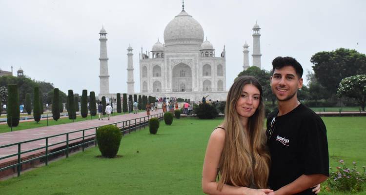 Ein junges Paar steht auf dem gepflegten Rasen mit dem Taj Mahal, der sich majestätisch hinter ihnen erhebt.