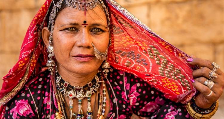 Porträt einer traditionell gekleideten Frau aus Rajasthan, die aufwendigen Schmuck und einen leuchtend roten Schleier zeigt.