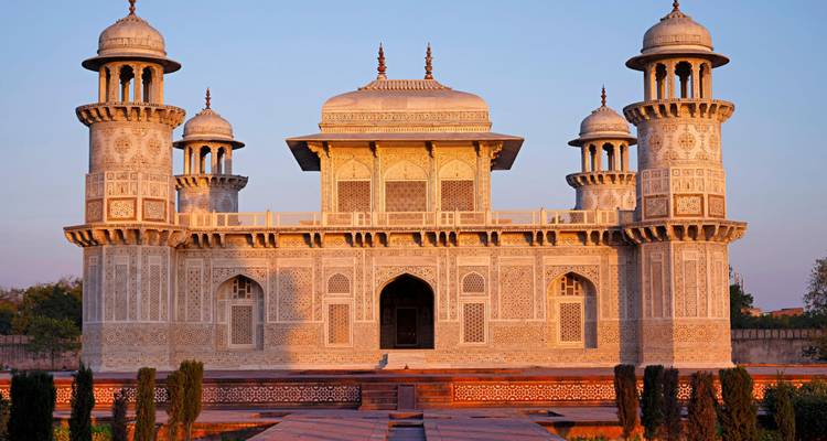Das zierlich gemeißelte Marmormausoleum von Itimad-ud-Daulah leuchtet in warmem Abendlicht in zartem Rosa gegen einen klaren Himmel.