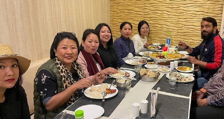 Friends gather around a long table enjoying an Indian meal inside a casual restaurant.