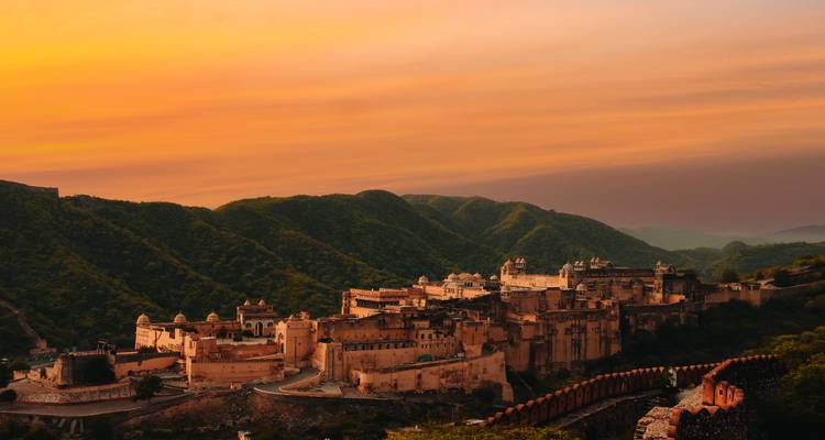 Amber Fort sprawls across green hills under a vivid orange sunset sky.