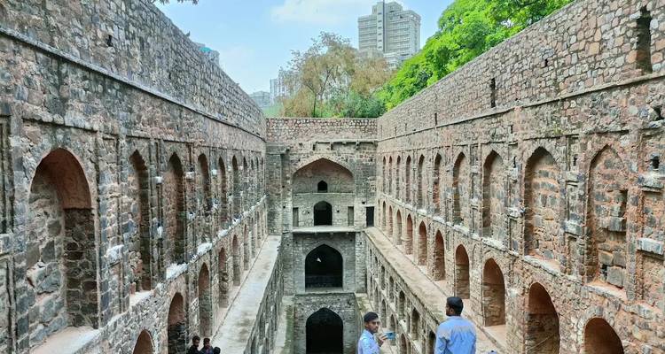 Visitors explore the deep stone arches of Agrasen Ki Baoli stepwell with city skyscrapers beyond.
