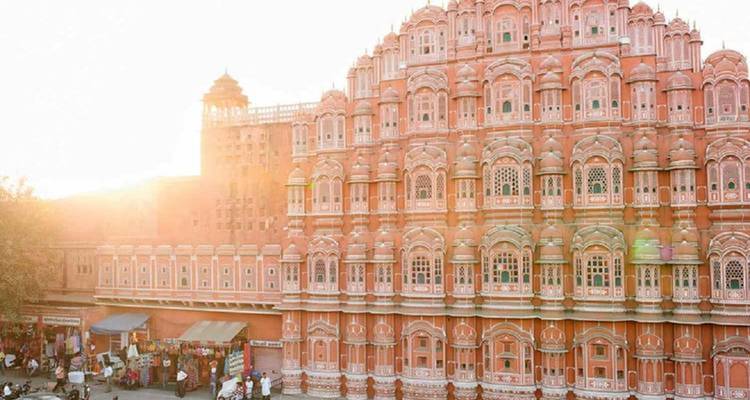 Sunlit façade of the pink sandstone Hawa Mahal rising over a busy street in the late afternoon.