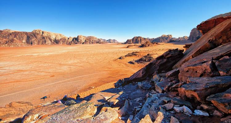 Vast red desert plain framed by rugged sandstone outcrops under a clear blue sky