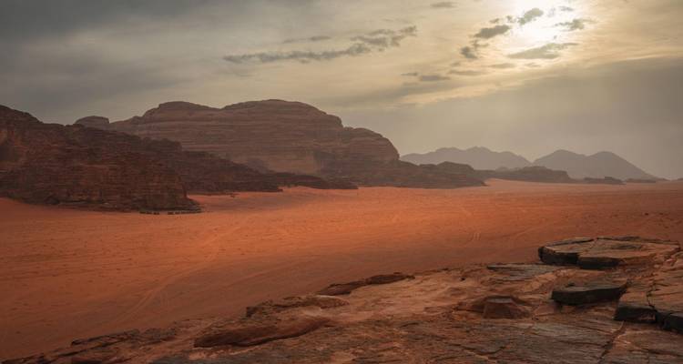 Moody late-day light casts long shadows over dusty red desert and looming rock formations