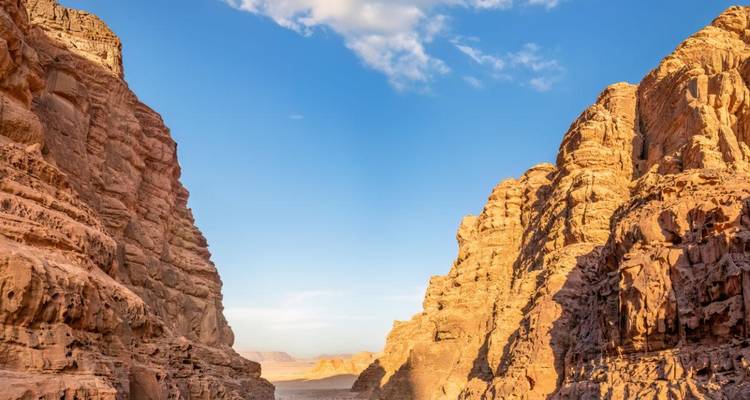 Steile Canyonwände aus sonnendurchflutetem Sandstein, die sich zu einem entfernten Tal unter blauem Himmel und Wolken öffnen.