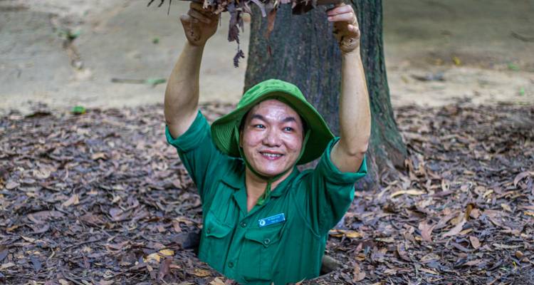Uniformed guide in green emerges smiling from a narrow tunnel entrance while holding leaf camouflage.
