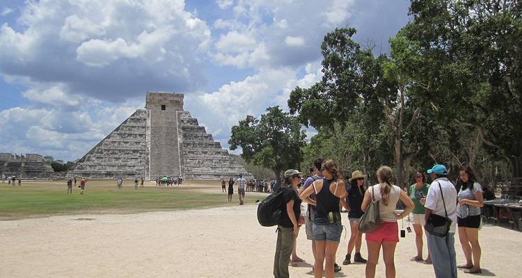 Toeristengroep luistert naar de gids voor de Chichen Itza piramide op een zonnige dag.