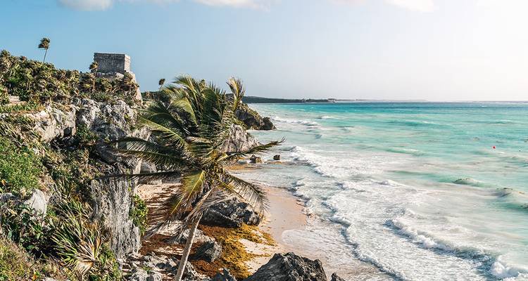 Turquoise Caribische golven breken tegen de rotsen onder de clifftop ruïnes van Tulum en palmbomen.