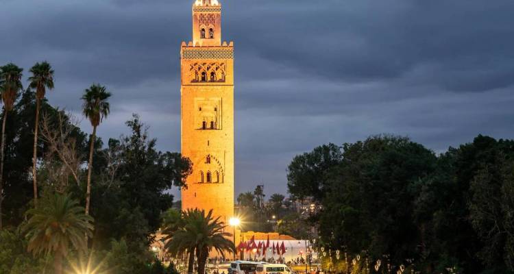 Le minaret de la Mosquée Koutoubia illuminé au crépuscule au-dessus des palmiers et de la rue animée à Marrakech