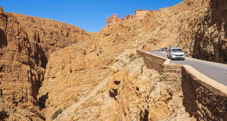 Le véhicule roule le long d'une route étroite épousant les falaises à travers un canyon rocheux sous un ciel bleu dégagé