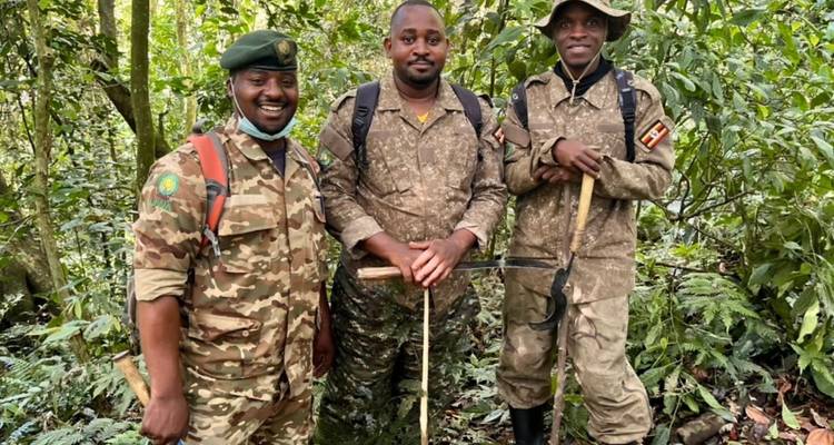 Three uniformed rangers carrying walking sticks stand together in dense rainforest.