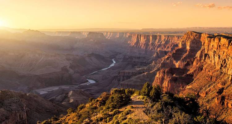 Adembenemend zonsopgangzicht over de Grand Canyon met gouden licht dat gelaagde rotswanden en de kronkelende Colorado River verlicht.