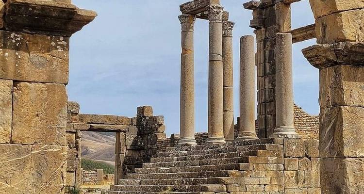 Goed bewaarde stenen zuilen en trappenhuizen van de antieke Romeinse plaats Volubilis onder een blauwe lucht.