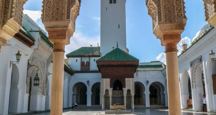 Binnenplaats van de Al-Qarawiyyin Moskee met sierlijke bogen die een centraal ritueel reinigingsfontein en groene tegeldaken omlijsten.
