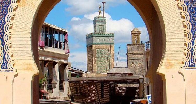 Uitzicht door decoratieve hufeisenboog naar mozaïektegels minaret en traditionele gebouwen in de medina van Fes.