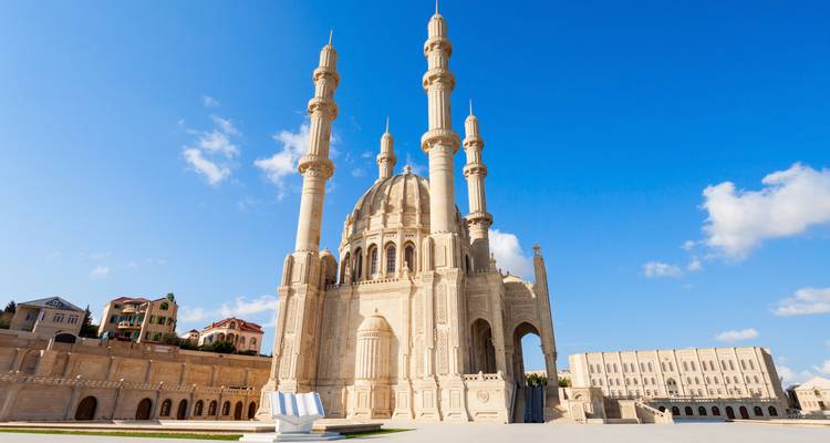 Elegant white stone mosque with four slender minarets rises against a perfectly clear blue sky.