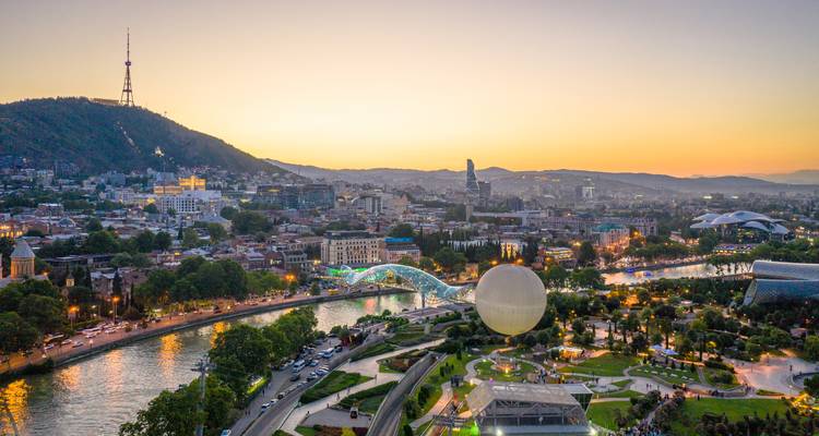 Panoramic sunset over Tbilisi with the river, Bridge of Peace and distant TV tower on the hill.