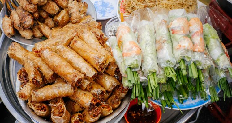 Straßenverkaufsstand mit gestapelten frittierten Frühlingsrollen und frischen Reispapierrollen gefüllt mit Garnelen und Kräutern.