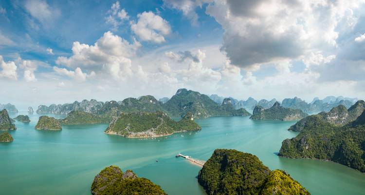 Hohe Panoramablick auf unzählige Kalksteininseln, die türkisfarbenes Wasser unter dramatischen Wolken in der Ha-Long-Bucht punktieren.