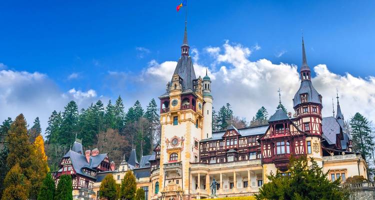Peles Castle with ornate towers set against a blue sky and forested hillside in Sinaia