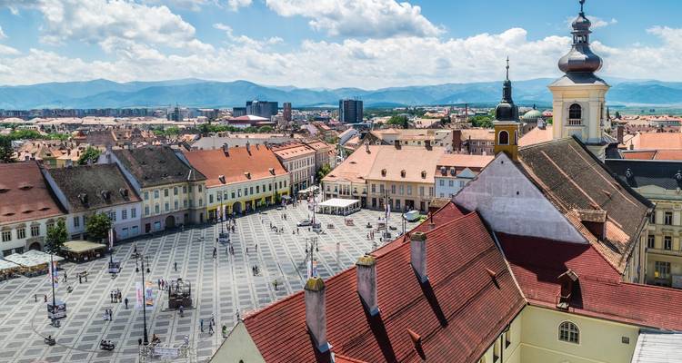 Aerial view of Sibiu’s large central square with pastel baroque buildings and mountains in the distance