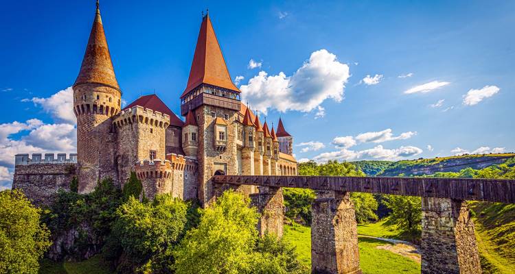Majestic Corvin Castle with red pointed roofs and a wooden bridge spanning a green gorge in Hunedoara