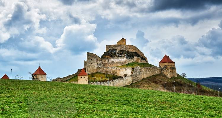 Rupea Fortress atop a grassy hill under dramatic clouds in Transylvania