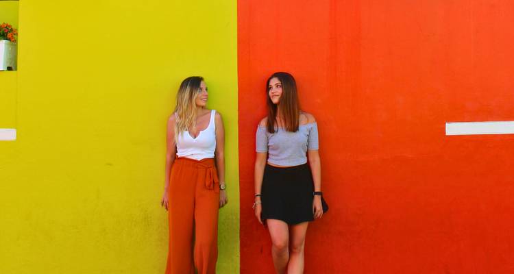Twee jonge vrouwen poseren tegen aangrenzende felgele en rode muren in Bo-Kaap.