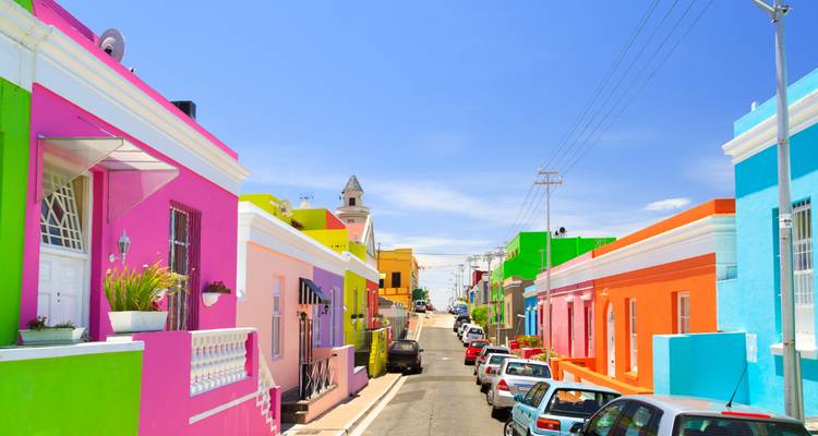 Kleurrijke rij huizen sieren de zonnige Bo-Kaap straat onder een stralend blauwe lucht.