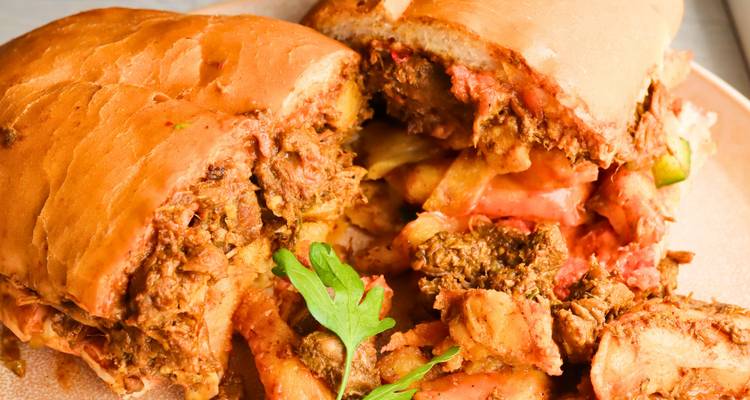 Close-up van een flinke pulled-meat sandwich vol patat en afgewerkt met verse groene kruiden.
