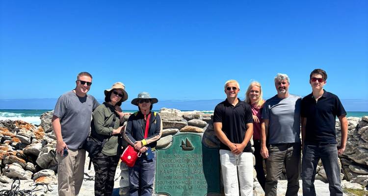 Des voyageurs posant à côté du monument de la pointe sud au cap Agulhas avec un océan et un ciel bleu vif en arrière-plan.