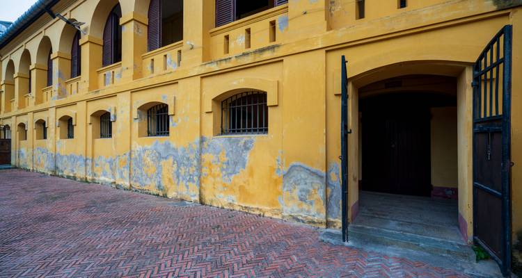 Verwitterte gelbe Aussenmauer des Hoa-Lo-Gefängnisses mit vergitterten Fenstern und abblätternder Farbe.