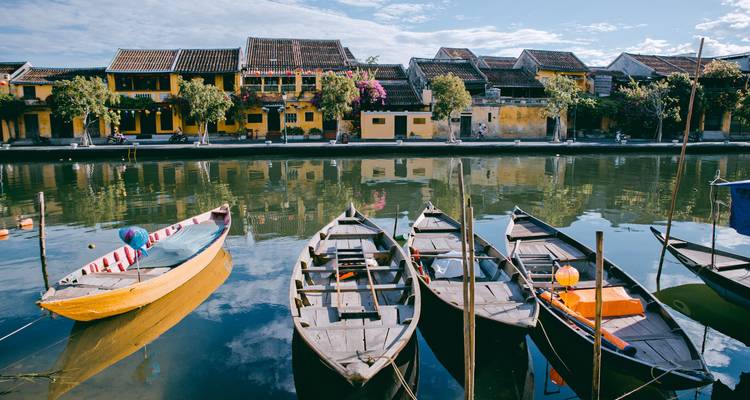 Ruhige Flussszene in Hoi An mit farbenfrohen Booten und gelben Heritage-Gebäuden, die sich im Wasser spiegeln.