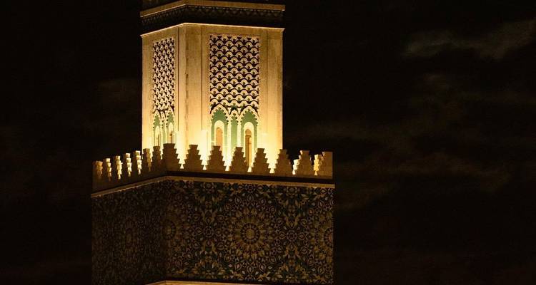 Night view of an ornately tiled minaret illuminated against a dark sky.