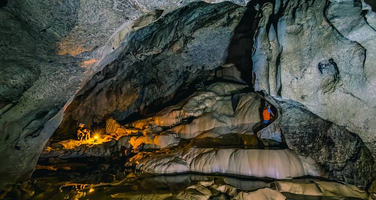 Illuminated limestone cave chamber with dramatic stalactites and flowstone formations.