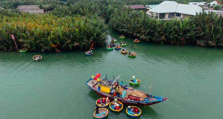 Aerial view of colourful basket boats flocking around a fishing vessel on a lush green canal.