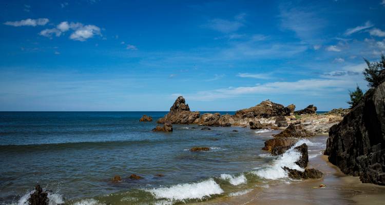 Rocky shoreline with gentle waves and deep blue sea under a bright sky.