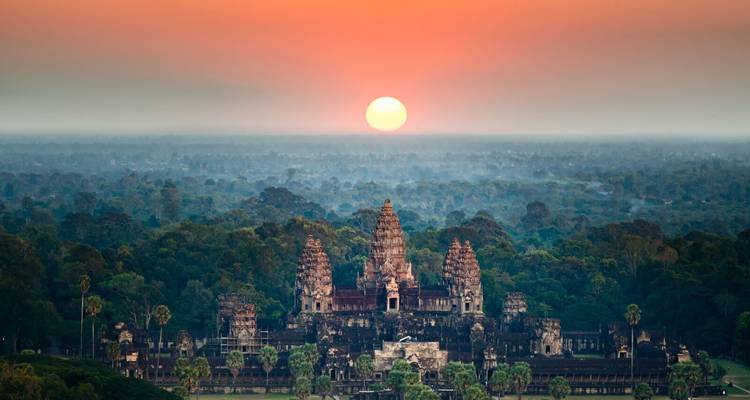 Angkor Wat framed by dense jungle under a rising sun casting warm light over the temples.