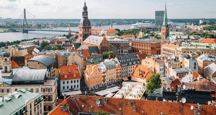 Punto de vista elevado sobre los tejados del casco antiguo de Riga, el río y los puentes lejanos bajo la luz suave del día.